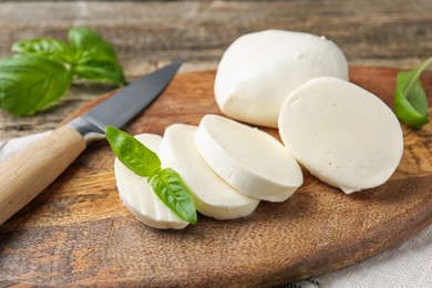 Photo of Cut mozzarella cheese with basil and knife on wooden table, closeup