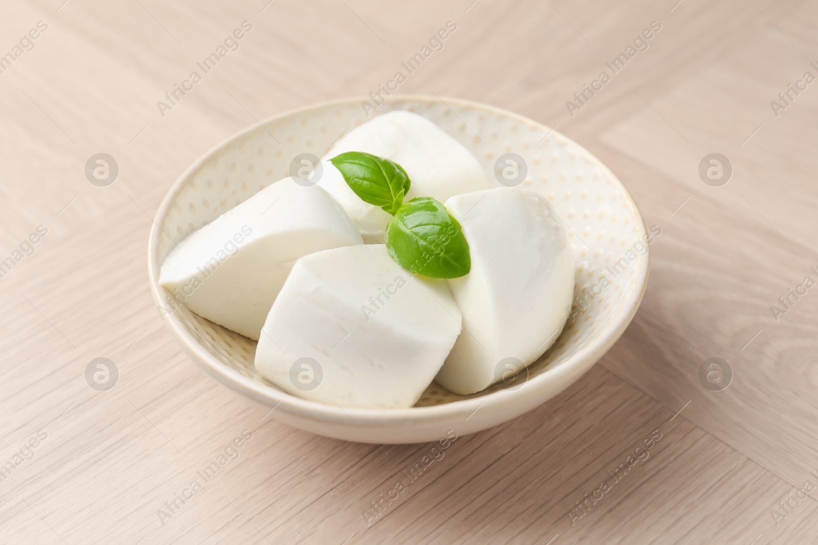 Pieces of delicious mozzarella cheese and basil in bowl on wooden table, closeup Photo of Pieces of delicious mozzarella cheese and basil in bowl on wooden table, closeup
