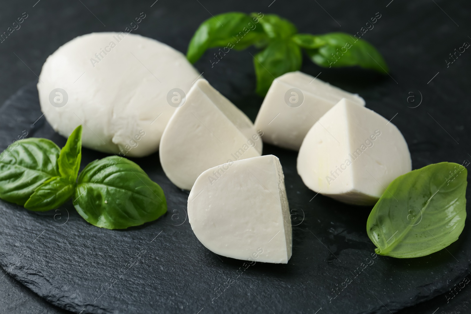 Pieces of delicious mozzarella cheese and basil on dark table, closeup Photo of Pieces of delicious mozzarella cheese and basil on dark table, closeup