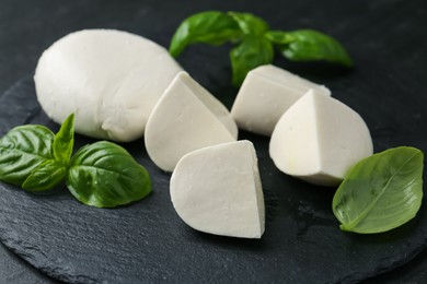 Photo of Pieces of delicious mozzarella cheese and basil on dark table, closeup