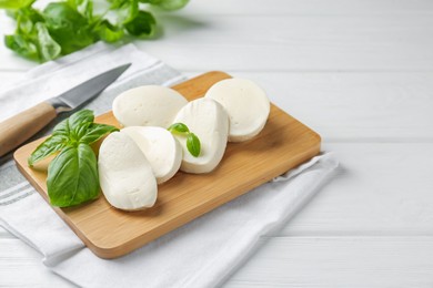 Photo of Pieces of delicious mozzarella cheese, basil leaves and knife on white wooden table, closeup