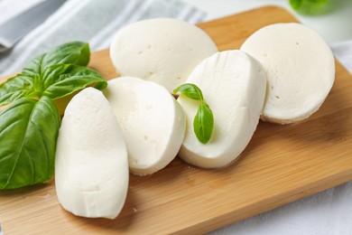 Photo of Pieces of delicious mozzarella cheese and basil leaves on table, closeup