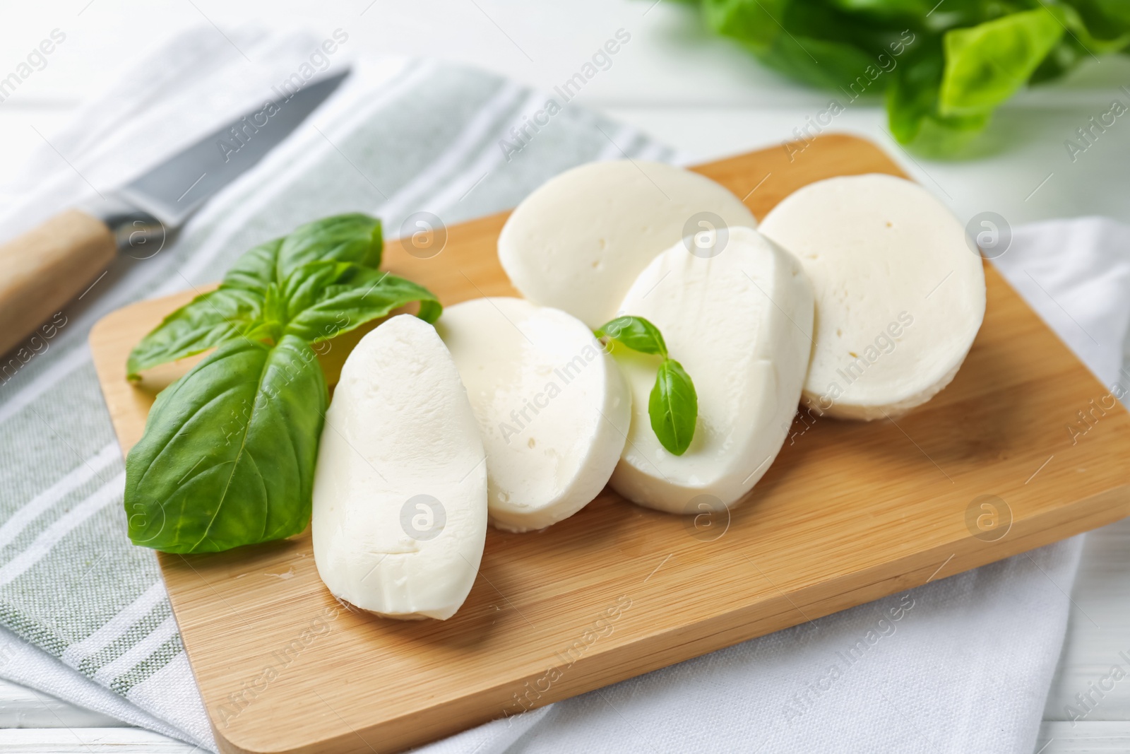 Pieces of delicious mozzarella cheese and basil leaves on white wooden table, closeup Photo of Pieces of delicious mozzarella cheese and basil leaves on white wooden table, closeup
