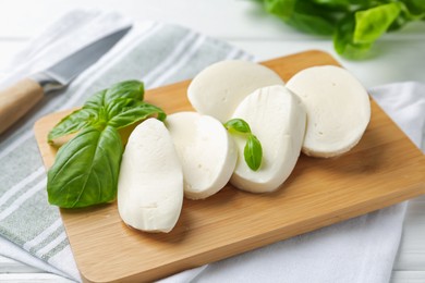 Photo of Pieces of delicious mozzarella cheese and basil leaves on white wooden table, closeup