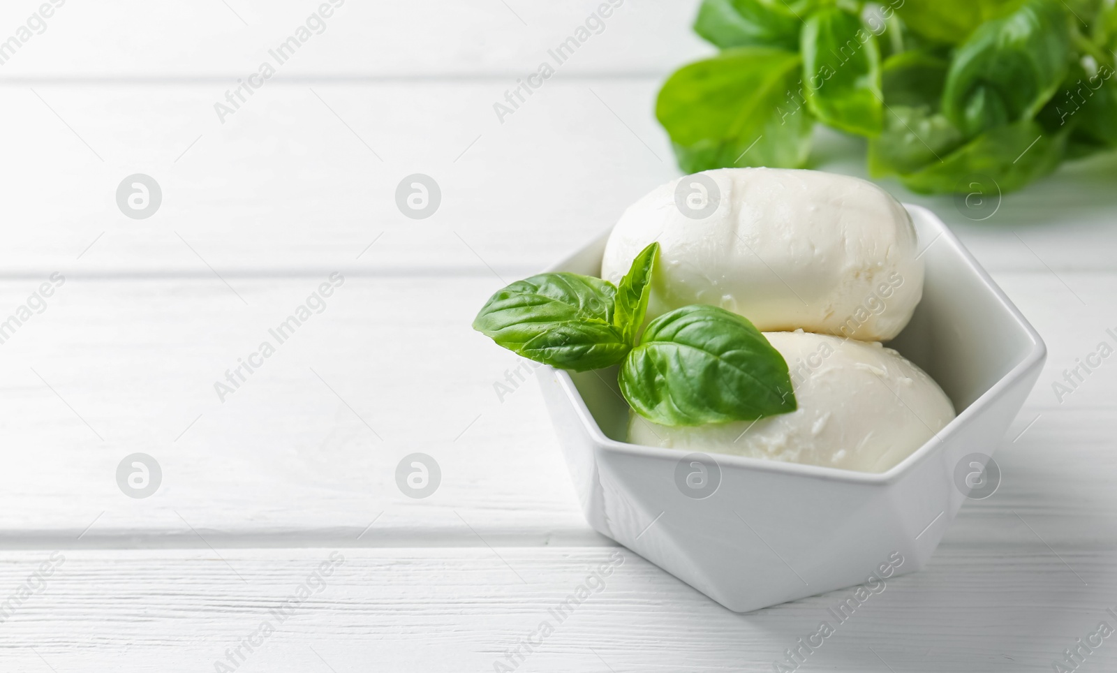 Pieces of delicious mozzarella cheese and basil in bowl on white wooden table, closeup. Space for text Photo of Pieces of delicious mozzarella cheese and basil in bowl on white wooden table, closeup. Space for text