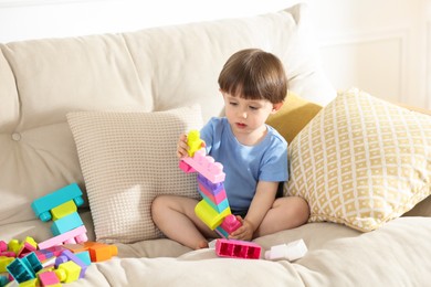 Photo of Cute little child playing with building bricks on sofa at home