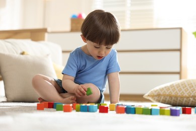 Photo of Cute little child playing with colorful cubes at home