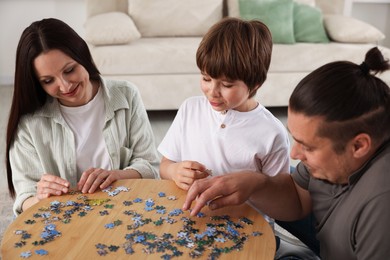 Photo of Parents with their son solving puzzle together at table indoors