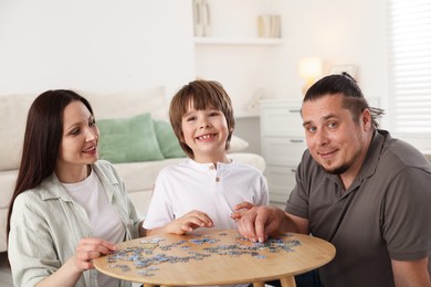 Photo of Parents with their son solving puzzle together at table indoors