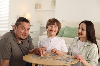 Photo of Parents with their son solving puzzle together at table indoors