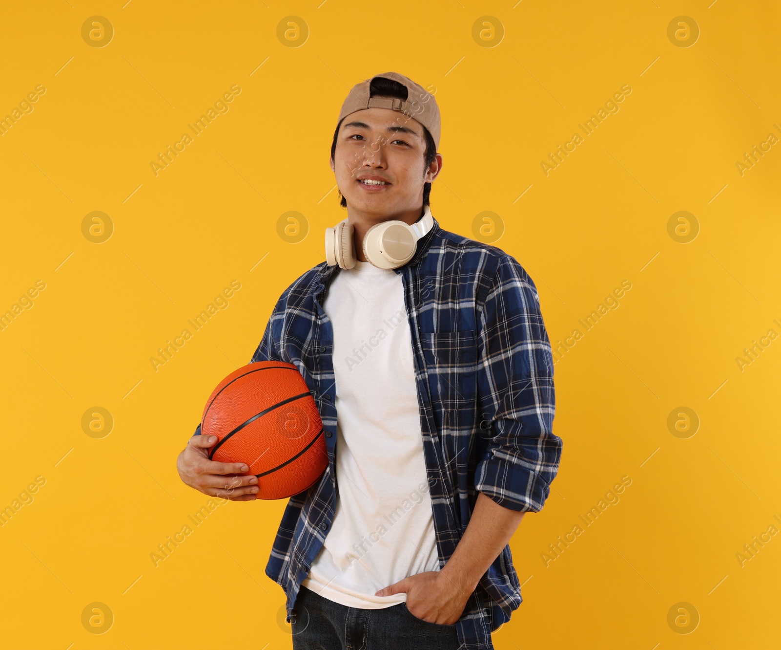 Student with headphones and basketball ball on orange background Photo of Student with headphones and basketball ball on orange background