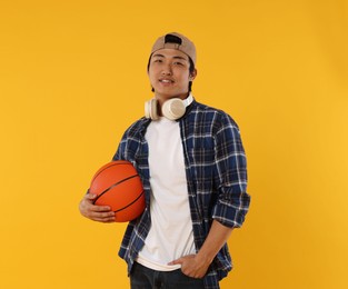 Photo of Student with headphones and basketball ball on orange background