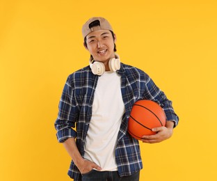 Photo of Student with headphones and basketball ball on orange background