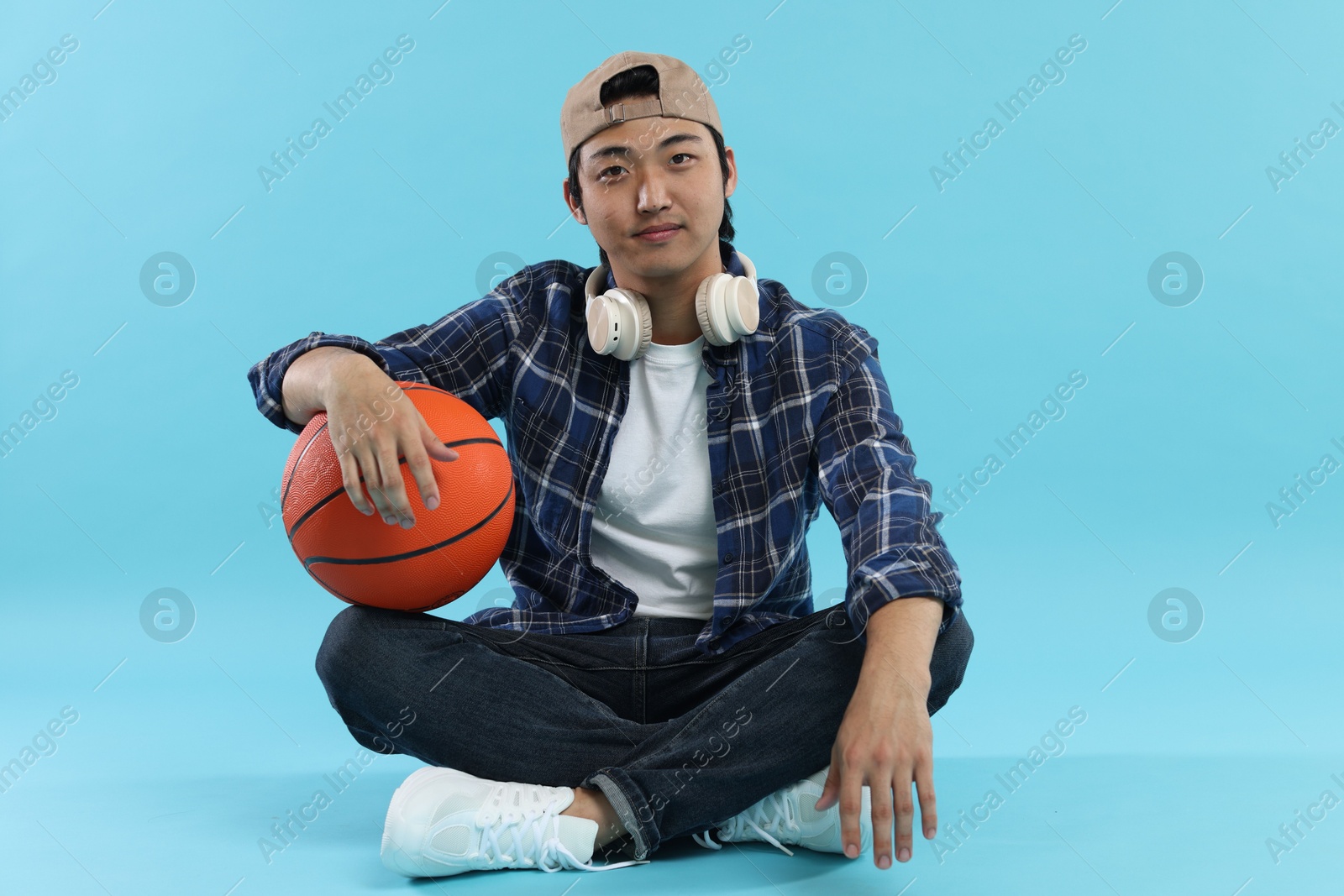 Student with headphones and basketball ball on light blue background Photo of Student with headphones and basketball ball on light blue background
