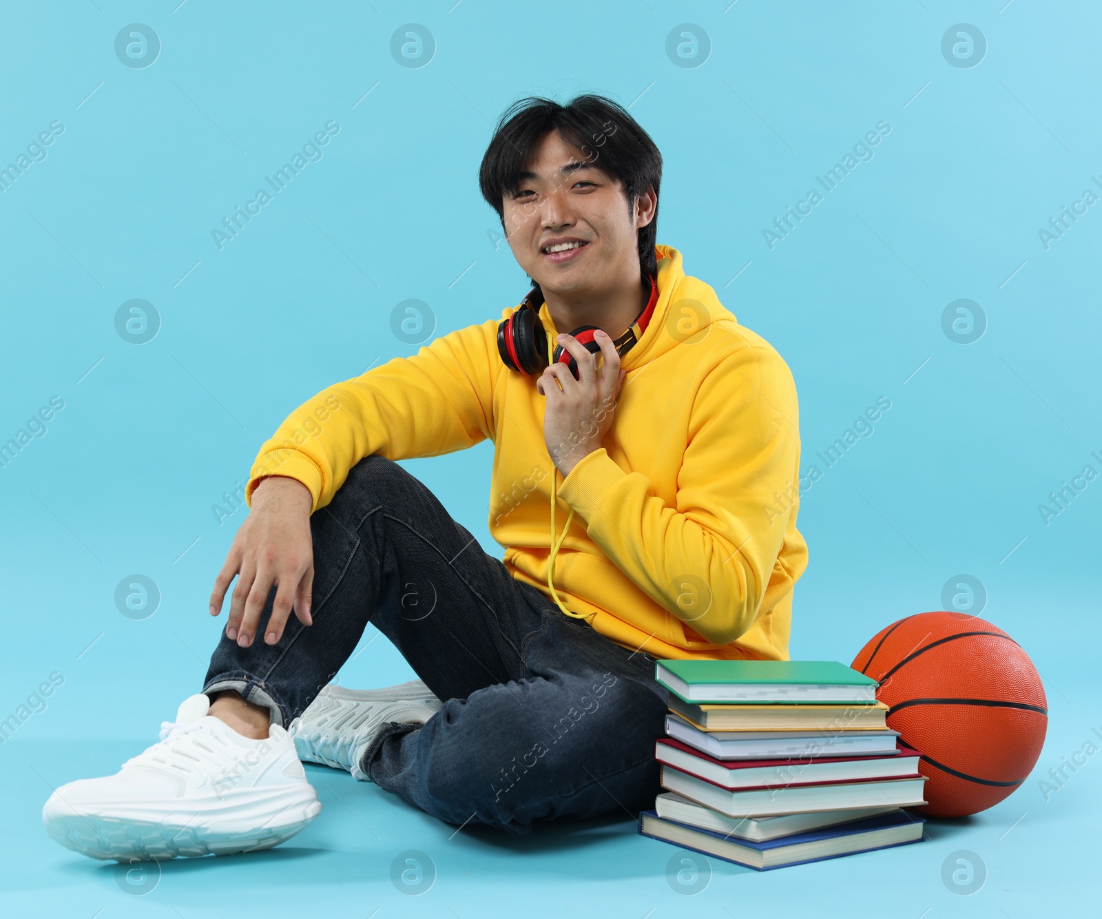 Photo of Student with books and basketball ball on light blue background