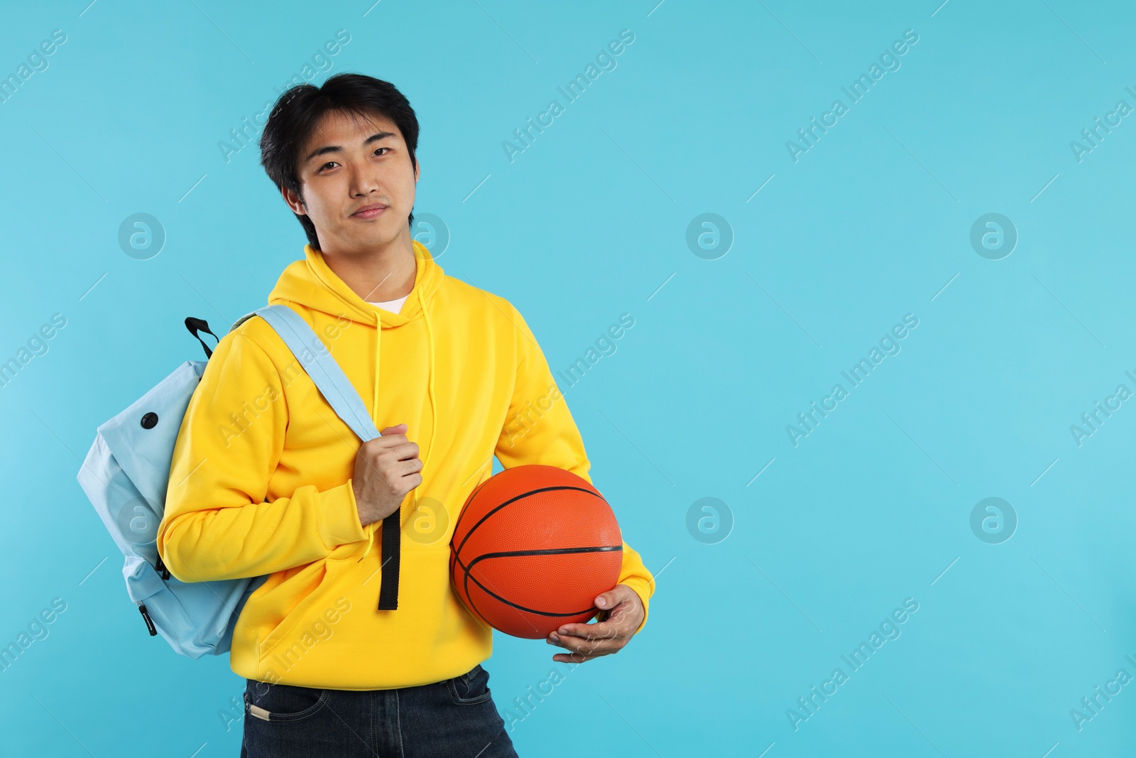 Photo of Student with basketball ball and backpack on light blue background, space for text