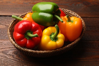 Photo of Fresh colorful bell peppers in wicker basket on wooden table, closeup