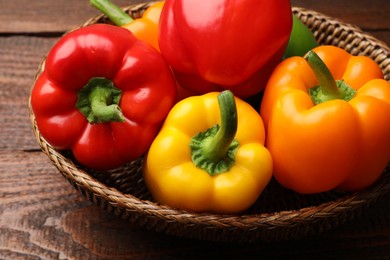 Photo of Fresh colorful bell peppers in wicker basket on wooden table, closeup