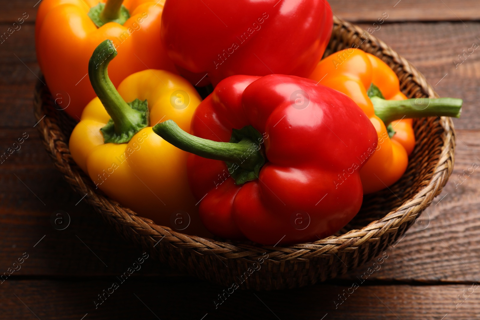 Fresh colorful bell peppers in wicker basket on wooden table, closeup Photo of Fresh colorful bell peppers in wicker basket on wooden table, closeup