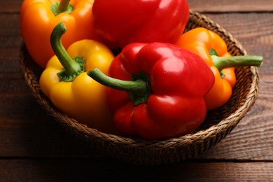 Photo of Fresh colorful bell peppers in wicker basket on wooden table, closeup