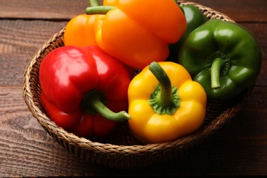 Photo of Fresh colorful bell peppers in wicker basket on wooden table, closeup