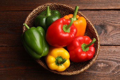 Photo of Fresh colorful bell peppers in wicker basket on wooden table, top view