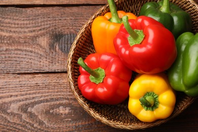 Photo of Fresh colorful bell peppers in wicker basket on wooden table, top view. Space for text