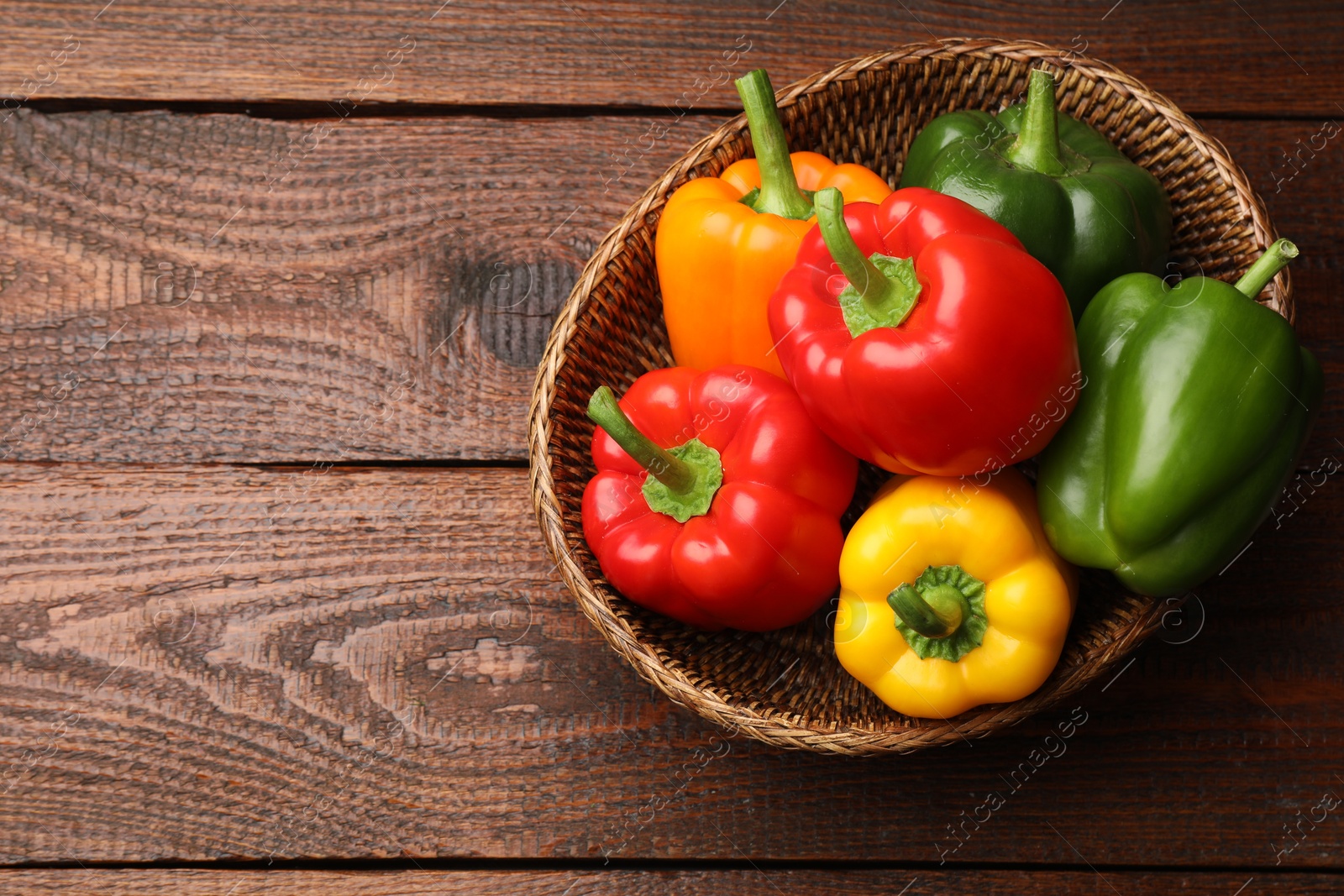 Fresh colorful bell peppers in wicker basket on wooden table, top view. Space for text Photo of Fresh colorful bell peppers in wicker basket on wooden table, top view. Space for text