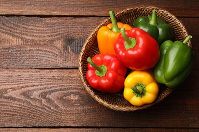 Photo of Fresh colorful bell peppers in wicker basket on wooden table, top view. Space for text