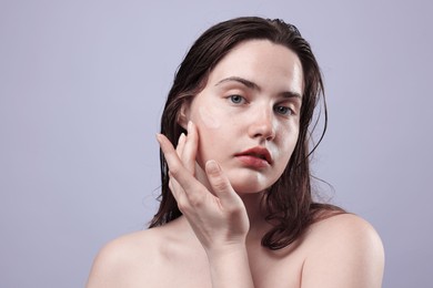 Photo of Portrait of woman with skincare product on her face against grey background, closeup