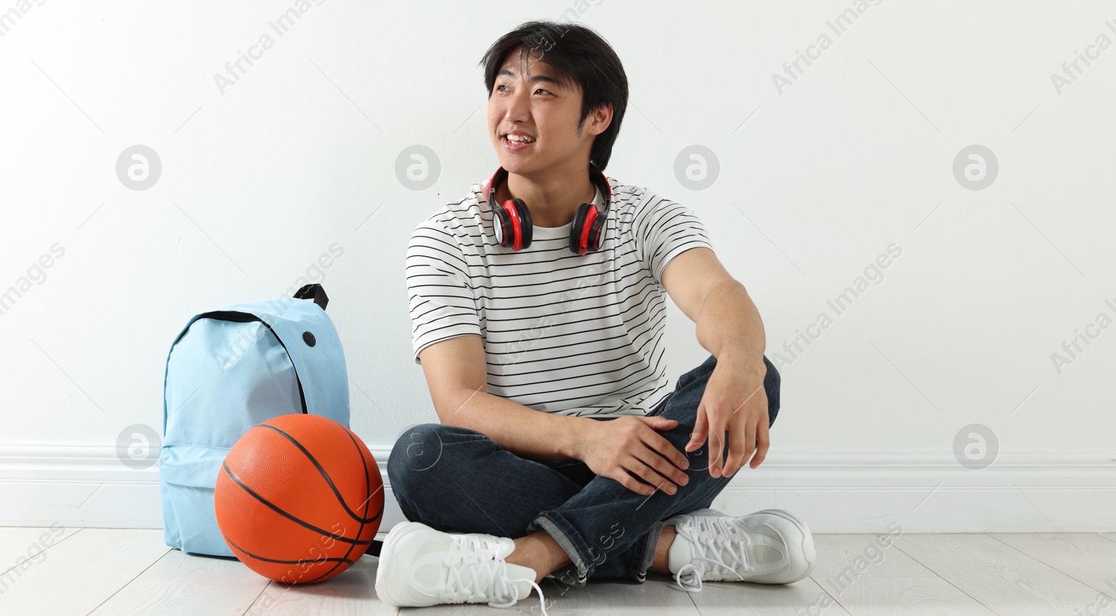 Photo of Happy student with basketball ball and backpack on floor indoors