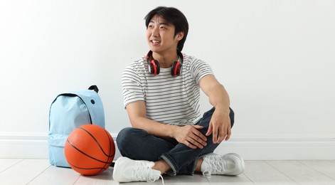 Photo of Happy student with basketball ball and backpack on floor indoors