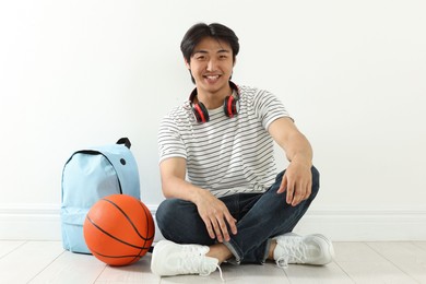 Photo of Happy student with basketball ball and backpack on floor indoors