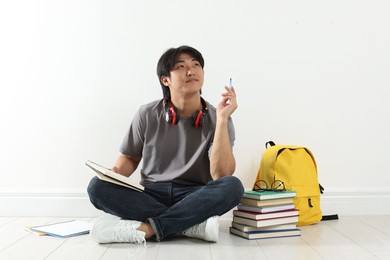 Photo of Student with notebook and pen studying on floor indoors