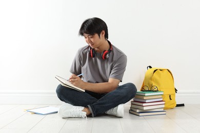 Photo of Student with notebook and pen studying on floor indoors