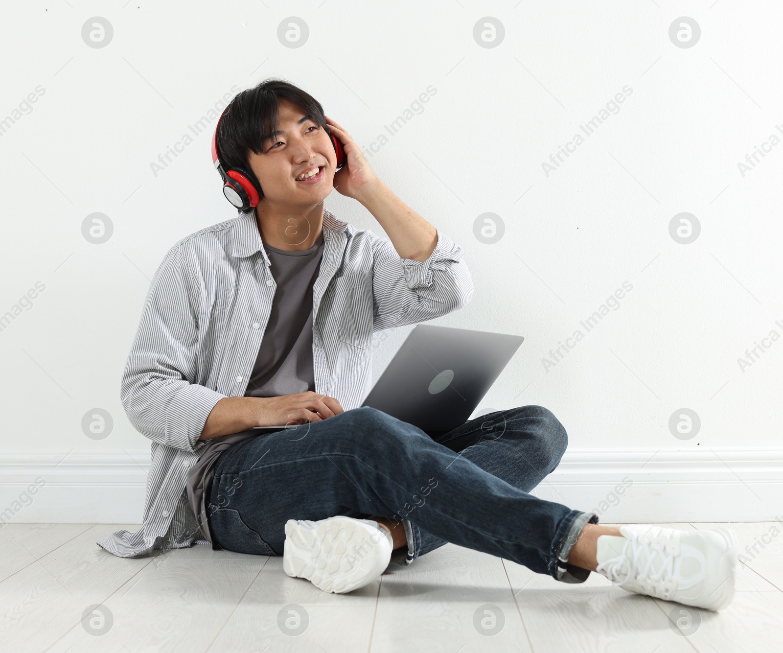 Student with headphones and laptop studying on floor indoors Photo of Student with headphones and laptop studying on floor indoors