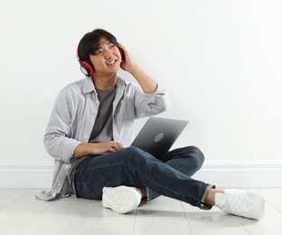Photo of Student with headphones and laptop studying on floor indoors