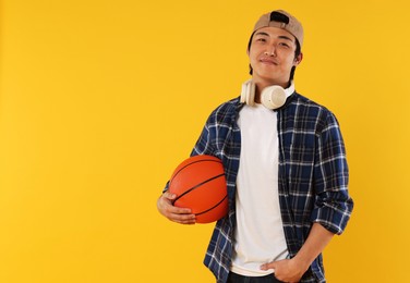 Photo of Student with headphones and basketball ball on orange background, space for text
