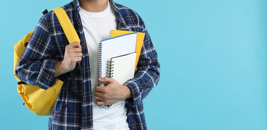 Photo of Student with backpack and notebooks on light blue background, closeup. Space for text