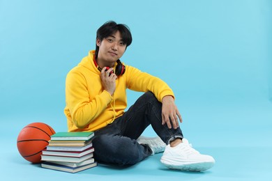 Photo of Student with books and basketball ball on light blue background