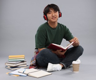 Photo of Student with headphones and book studying on grey background