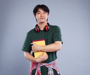 Photo of Student with headphones and books on grey background
