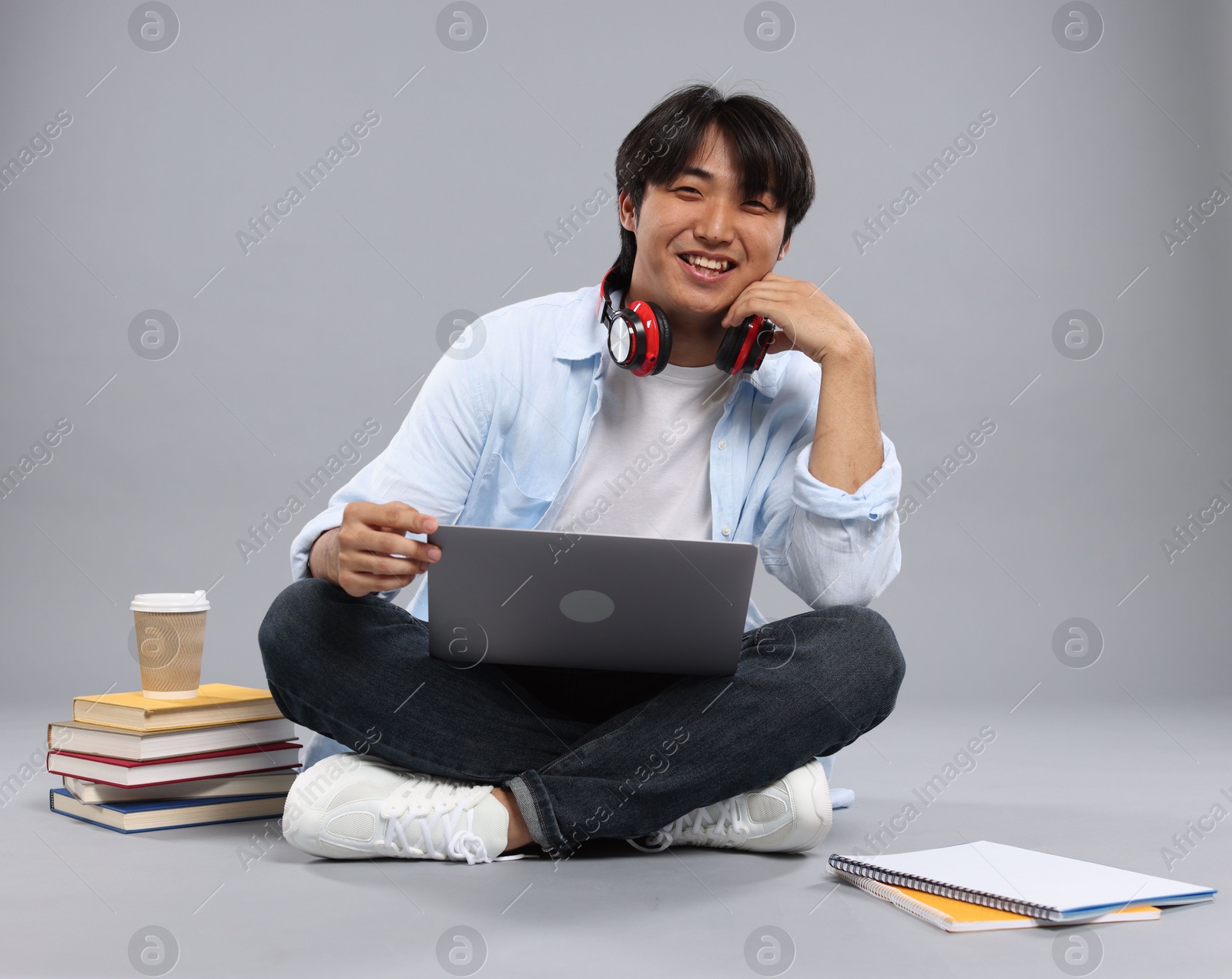 Student with headphones and laptop on grey background Photo of Student with headphones and laptop on grey background