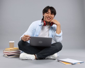 Photo of Student with headphones and laptop on grey background
