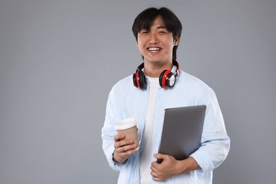 Photo of Student with headphones, coffee and laptop on grey background, space for text