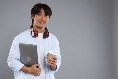 Photo of Student with headphones, coffee and laptop on grey background, space for text