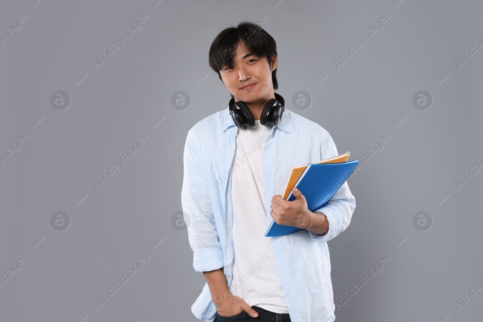 Student with headphones and notebooks on grey background Photo of Student with headphones and notebooks on grey background