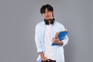 Photo of Student with headphones and notebooks on grey background