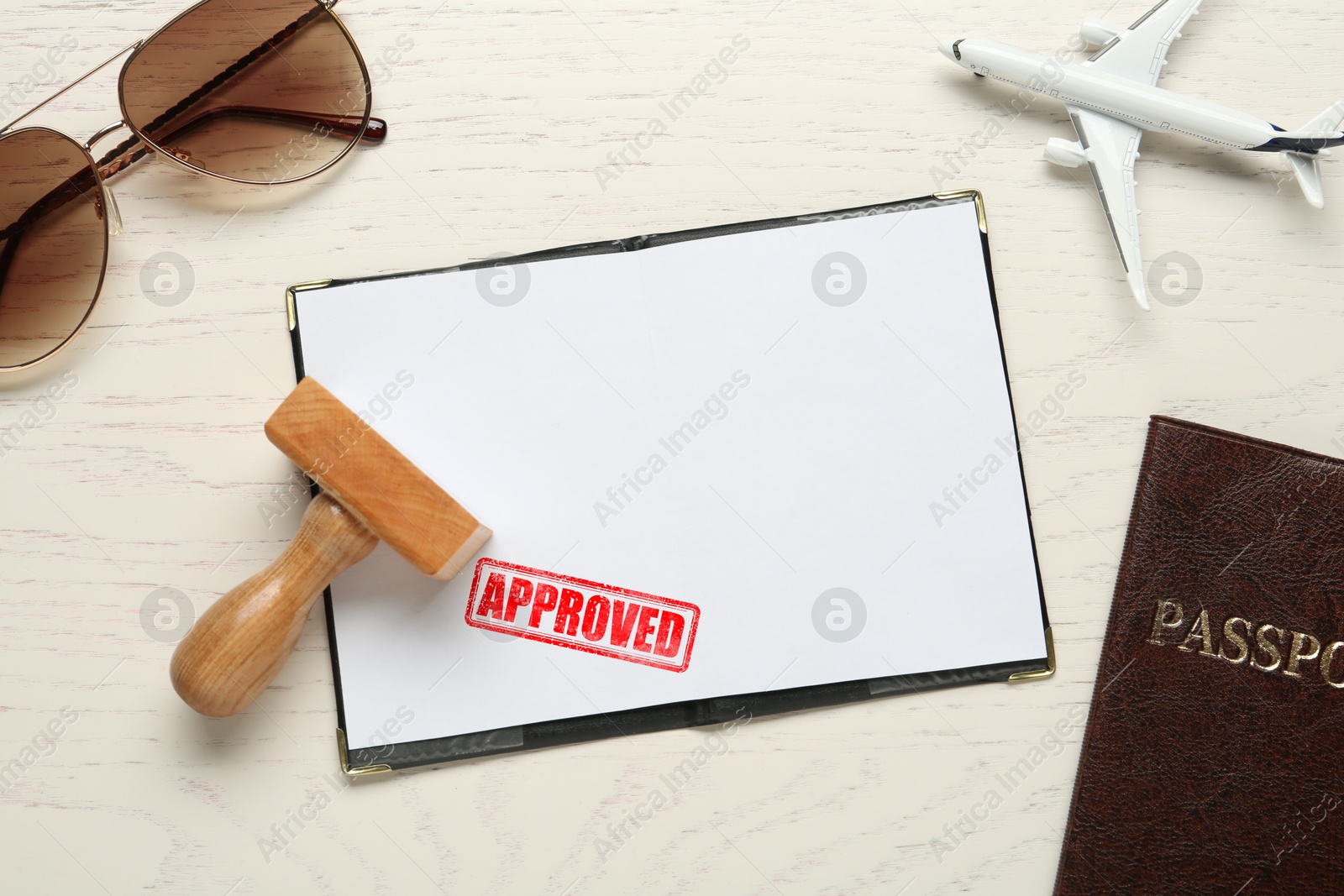 Image of Red stamp Approved in passport. Flat lay composition with toy plane, passports and wooden stamp on table