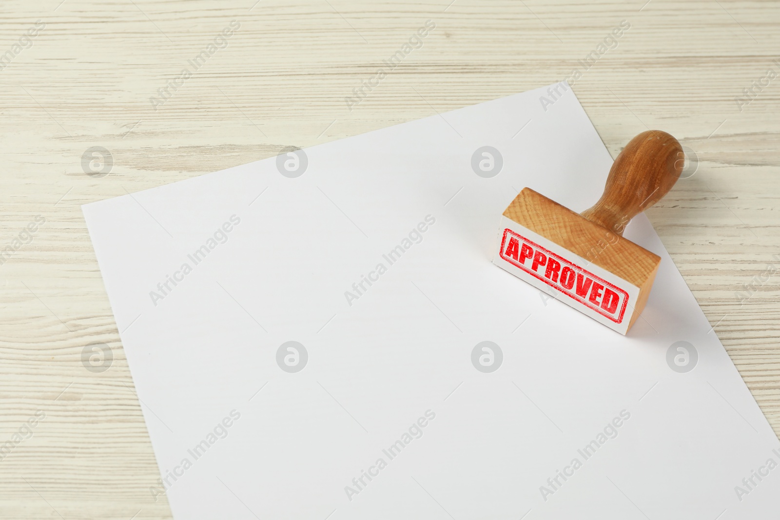 Wooden stamp with word Approved and blank sheet of paper on table Image of Wooden stamp with word Approved and blank sheet of paper on table